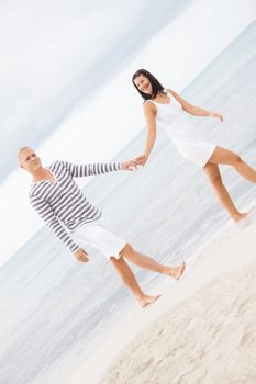 Caucasian happy young couple holding hands while walking barefoot on the beach in a romantic travel destination