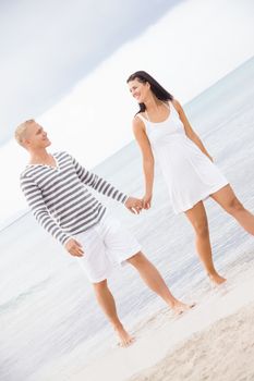 Caucasian happy young couple holding hands while walking barefoot on the beach in a romantic travel destination