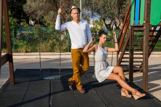 Elegant trendy young couple in fashionable modern clothes and accessories posing outdoors in the summer sunshine in a garden or park