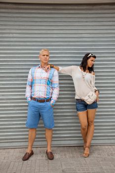 Fashionable young couple in trendy clothes posing in front of a metal door with the woman leaning on the mans shoulder