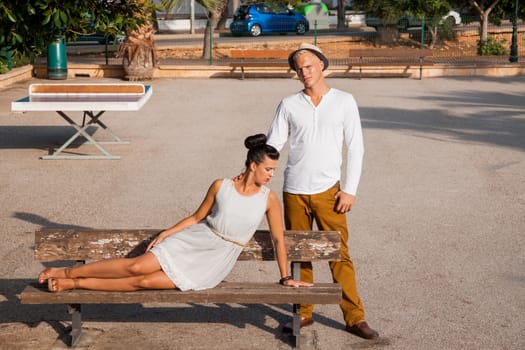 Elegant trendy young couple in fashionable modern clothes and accessories posing outdoors in the summer sunshine in a garden or park