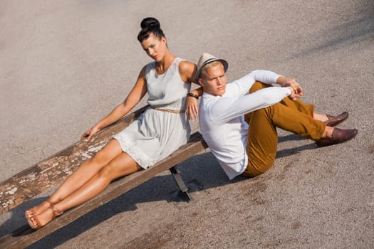 Elegant trendy young couple in fashionable modern clothes and accessories posing outdoors in the summer sunshine in a garden or park