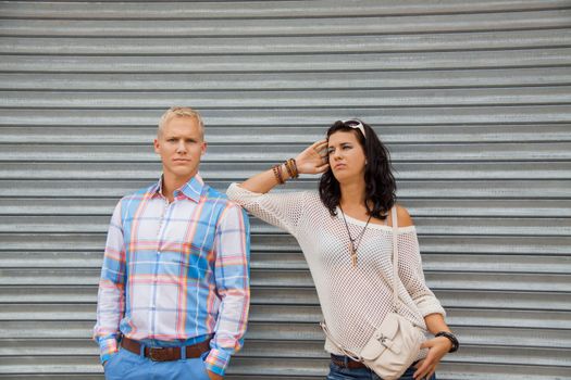 Fashionable young couple in trendy clothes posing in front of a metal door with the woman leaning on the mans shoulder