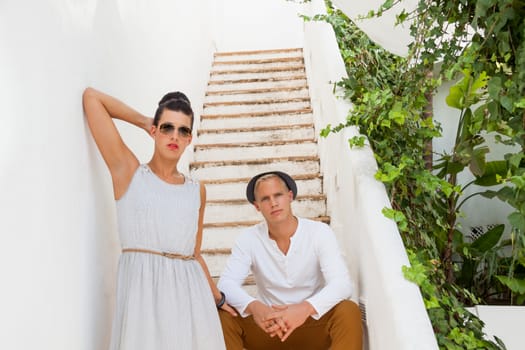 Elegant trendy young couple in fashionable modern clothes and accessories posing outdoors in the summer sunshine in a garden or park