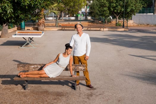 Elegant trendy young couple in fashionable modern clothes and accessories posing outdoors in the summer sunshine in a garden or park