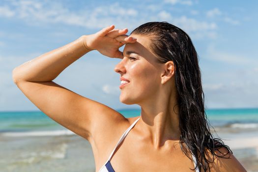 Young woman smiling looking far away shading her eyes with her hand in the beach
