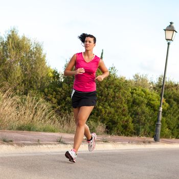 Determined fit young Caucasian woman practicing jogging in the park, in a warm summer day