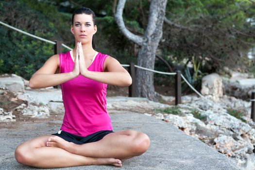 Attractive young woman with a serene expression sitting barefoot meditating in the lotus position outdoors in a park