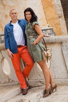 Young attractive couple in summer fashion standing together on the shallow stone steps of a bridge looking back at the camera with serious expressions, candid natural shot