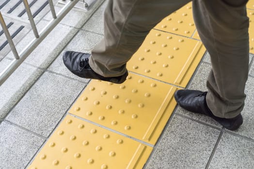 Man legs are crossing the yellow line on the train station, danger