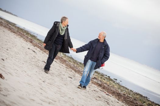 mature happy couple walking on beach in autumn lifestyle healthy