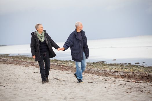 mature happy couple walking on beach in autumn lifestyle healthy