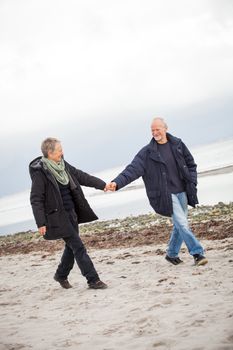 mature happy couple walking on beach in autumn lifestyle healthy