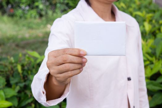 woman's hand showing business card - closeup shot on garden background.
