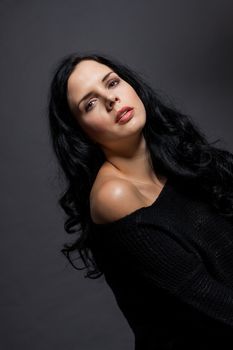 Dark moody portrait of a sultry beautiful woman with long black hair wearing a stylish off the shoulder top , head and shoulders against a grey studio background