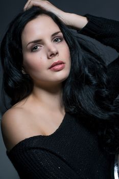 Dark moody portrait of a sultry beautiful woman with long black hair wearing a stylish off the shoulder top , head and shoulders against a grey studio background