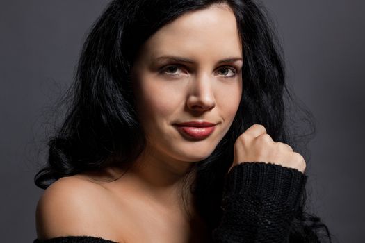 Dark moody portrait of a sultry beautiful woman with long black hair wearing a stylish off the shoulder top , head and shoulders against a grey studio background