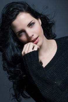 Dark moody portrait of a sultry beautiful woman with long black hair wearing a stylish off the shoulder top , head and shoulders against a grey studio background