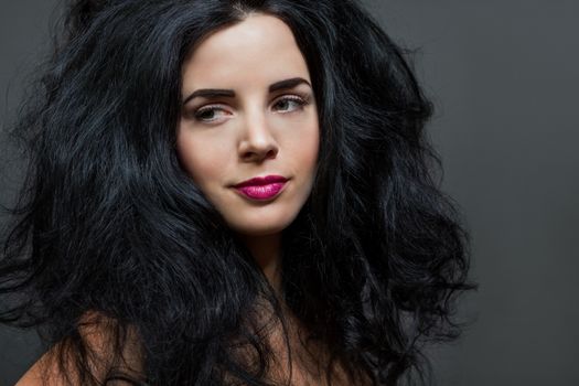 Atmospheric studio portrait of a beautiful black haired woman with a gentle serene expression gazing over her naked shoulder directly at the camera, close up head and shoulders against black