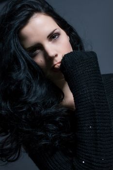 Dark moody portrait of a sultry beautiful woman with long black hair wearing a stylish off the shoulder top , head and shoulders against a grey studio background