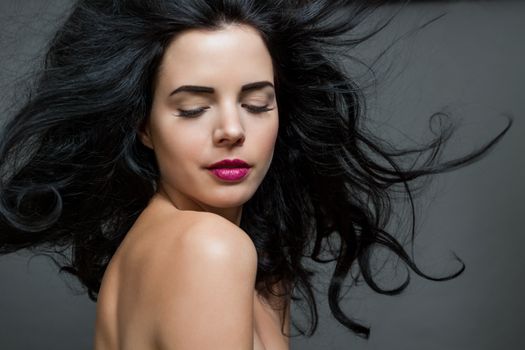 Atmospheric studio portrait of a beautiful black haired woman with a gentle serene expression gazing over her naked shoulder directly at the camera, close up head and shoulders against black