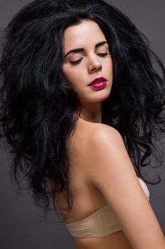 Atmospheric studio portrait of a beautiful black haired woman with a gentle serene expression gazing over her naked shoulder directly at the camera, close up head and shoulders against black