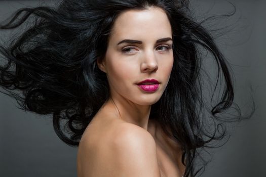 Atmospheric studio portrait of a beautiful black haired woman with a gentle serene expression gazing over her naked shoulder directly at the camera, close up head and shoulders against black