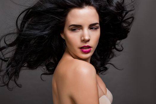 Atmospheric studio portrait of a beautiful black haired woman with a gentle serene expression gazing over her naked shoulder directly at the camera, close up head and shoulders against black