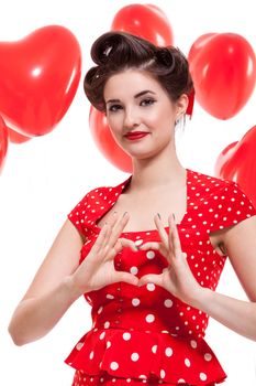 Beautiful retro woman with a French roll hairstyle celebrating Valentines Day dressed in a red polka dot dress and holding a red heart while looking at the camera with a gentle smile