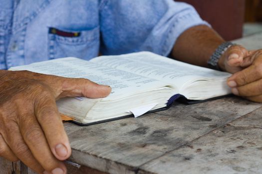 Thai old man reading bible on wooden table, focusing on bible