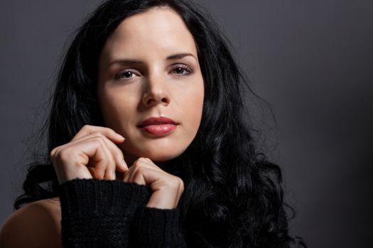 Dark moody portrait of a sultry beautiful woman with long black hair wearing a stylish off the shoulder top , head and shoulders against a grey studio background