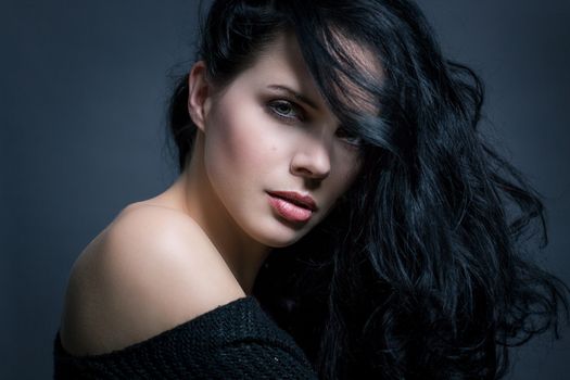 Dark moody portrait of a sultry beautiful woman with long black hair wearing a stylish off the shoulder top , head and shoulders against a grey studio background