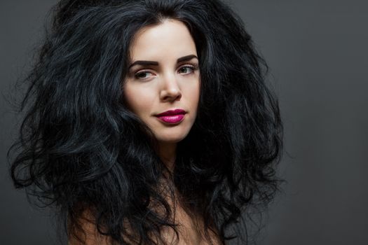 Atmospheric studio portrait of a beautiful black haired woman with a gentle serene expression gazing over her naked shoulder directly at the camera, close up head and shoulders against black