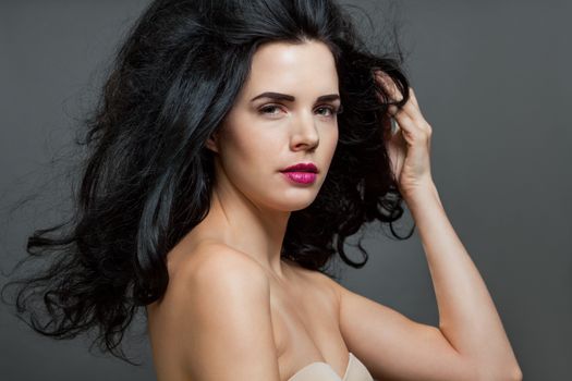 Atmospheric studio portrait of a beautiful black haired woman with a gentle serene expression gazing over her naked shoulder directly at the camera, close up head and shoulders against black