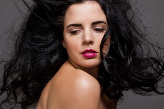 Atmospheric studio portrait of a beautiful black haired woman with a gentle serene expression gazing over her naked shoulder directly at the camera, close up head and shoulders against black