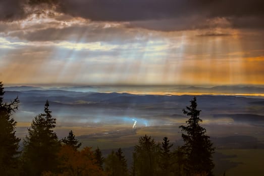 Godly light rays passing through clouds in the early morning above hilly countryside
