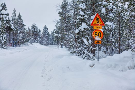 Warning traffic sign, warning skier and snowmobile sign on snowy arctic winter forest.