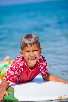 Happy Young boy having fun at the beach on vacation with surfboard
