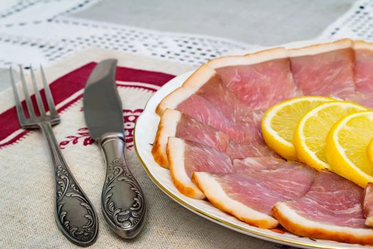 Delicious slices of ham and lemon on the plate, next Cutlery: knife and fork.