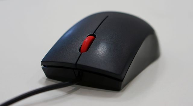 Computer mouse has a black wire attached to the PC, scrolling button is red in the middle.                 