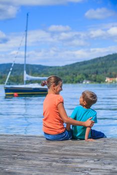 Summer vacation  at the lake - two happy kids resting on the pier and watching on the yacht
