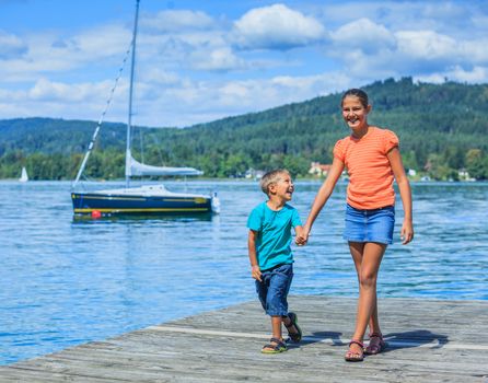 Summer vacation  at the lake - two happy kids walking on the pier and watching on the yacht
