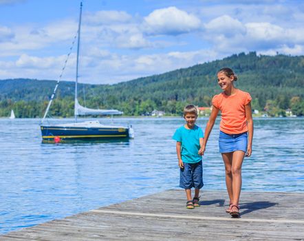 Summer vacation  at the lake - two happy kids walking on the pier and watching on the yacht