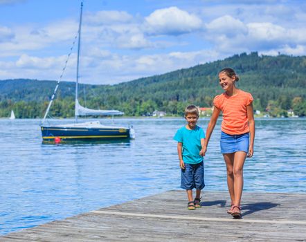 Summer vacation  at the lake - two happy kids walking on the pier and watching on the yacht