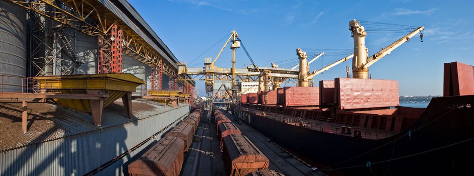 Grain from silos being loaded onto cargo ship on conveyor belt with freight train