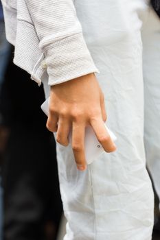 hand of woman holding white mobile phone on the side of her leg.