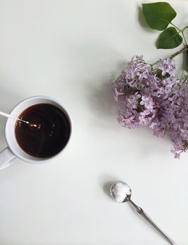 Milk pouring into coffee with sugar spoon and fresn lilac flowers