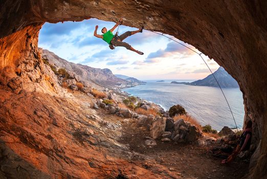 Male rock climber climbing along a roof in a cave at sunset