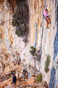 Young woman lead clYoung woman lead climbing on natural cliff, belayer watching her mbing on natural cliff, belayer watching her
