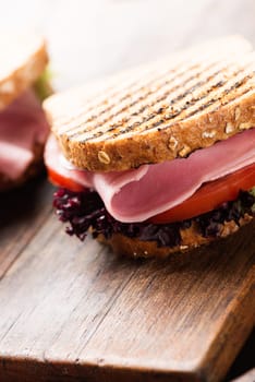 Sandwich with ham, salad, tomato on wooden table